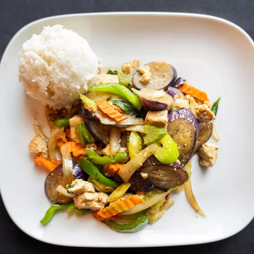 A white plate with a scoop of white rice and a stir-fry of eggplant, tofu, and vegetables.