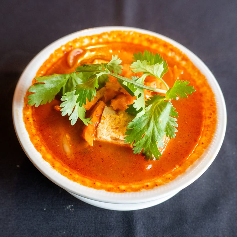 Close-up of a white bowl filled with vibrant orange-red soup, tofu, and fresh cilantro.