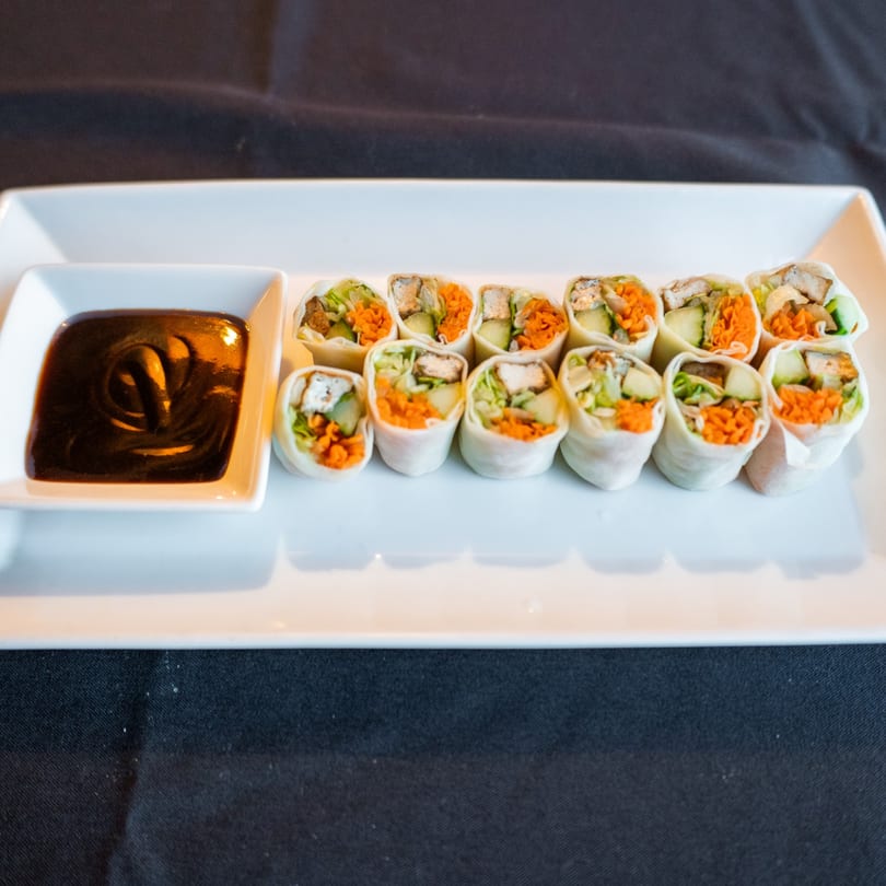 Spring rolls with chicken, carrots, and lettuce, served with a side of dark dipping sauce.