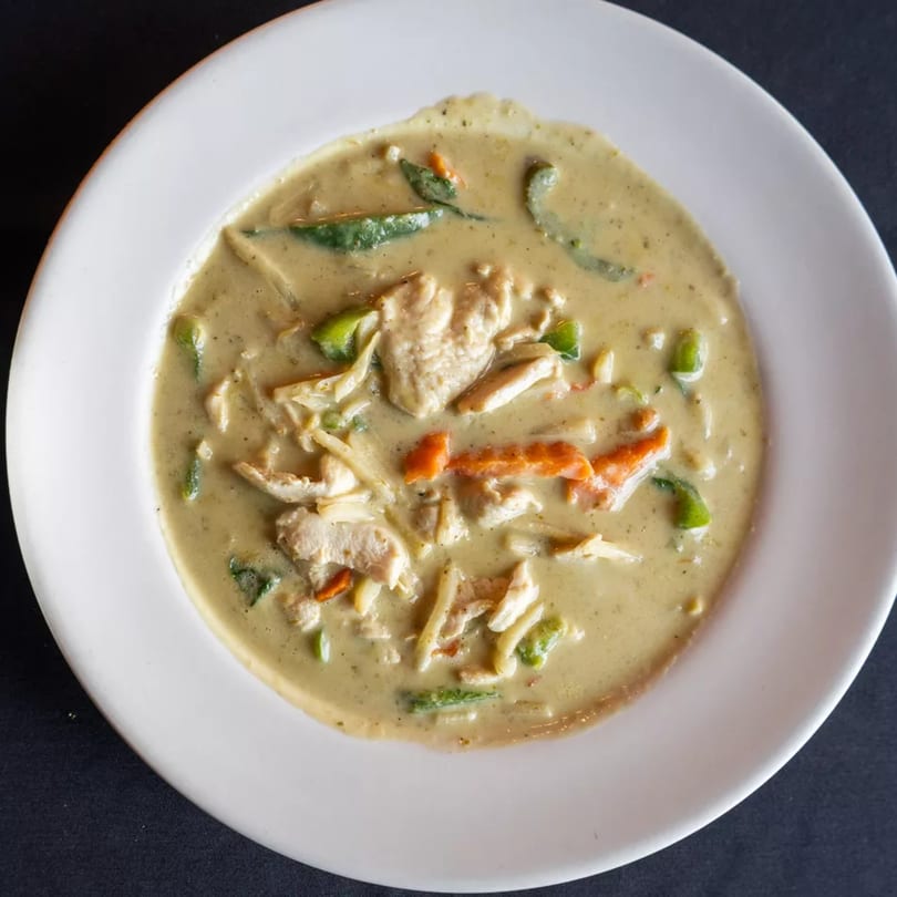 Creamy green curry with chicken, bell peppers, and bamboo shoots in a white bowl.